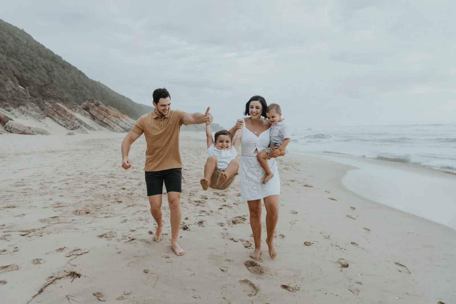 Parents swing their child between them during a family walk on the beach