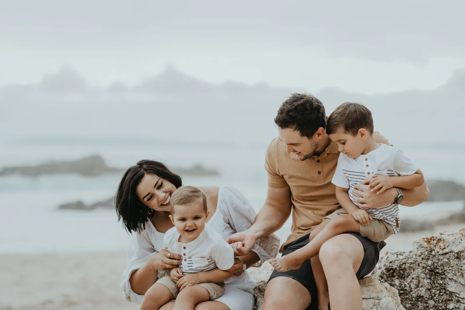 Parents sit with their two children on rocks above the beach