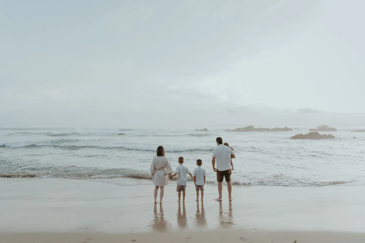 A family of four stands together looking out to sea