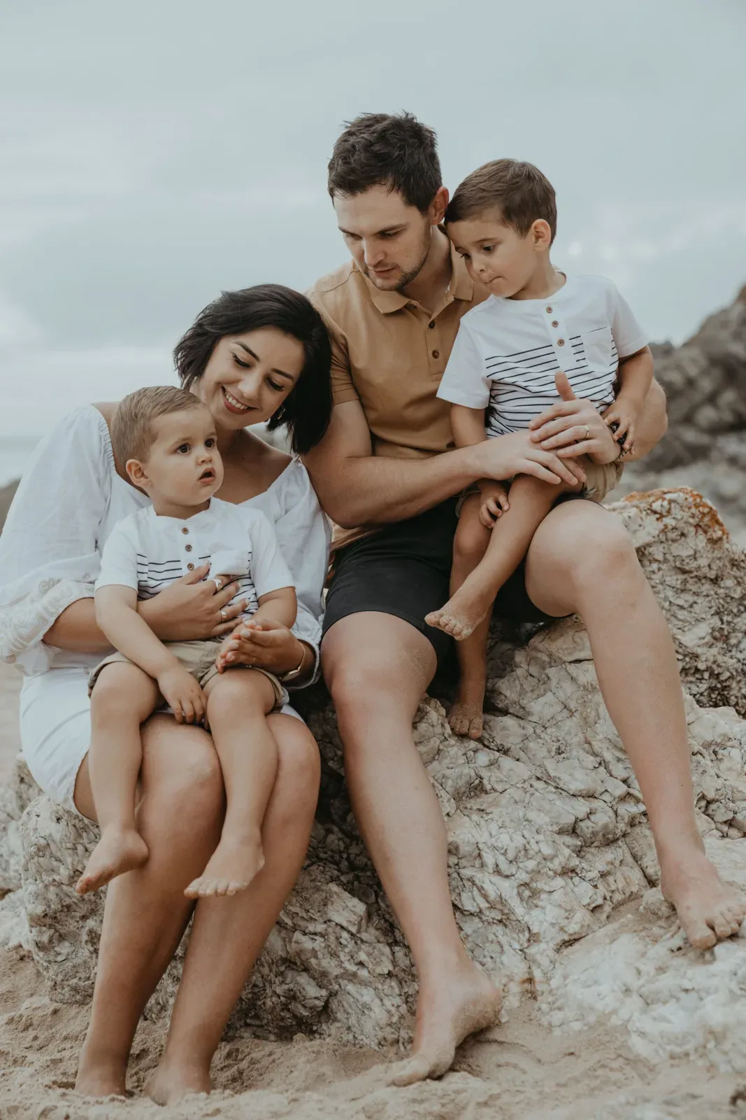 A family cuddles together on rocks beside the beach in Plettenberg Bay